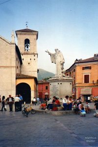 belebte Piazza mit handweisender Skulptur San Benedetto, Nórcia