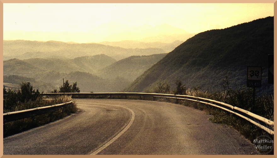 Straßenkurve mit Leitplanke über endloser Hügelkette zwischen Albaneto und Posta, sepiafarben