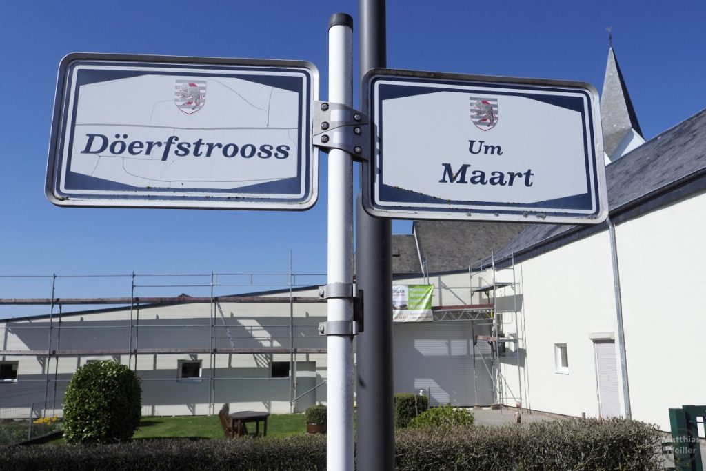 Schilder "Döerfstroos" und "Um Maart" Nahaufnahme vor Kirchturm