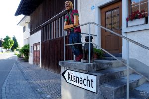 Holshcnitzfigur und Hund über Richtungsschild "Küsnacht" in Forch