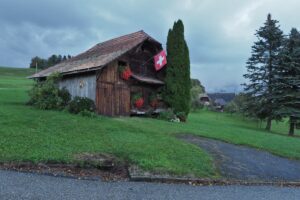 Hüttenhaus mit Blumenshcmuck und Schweizer Flagge, tief hängende Wolken