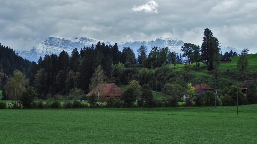 Schneebedeckte Schrattenluh vor grüner Bergwiese mit Bauernhaus und Tannewald