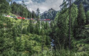 Bahnviadukt mit Bahn rot/weiß, mit Lärchenwald und Berggipfel