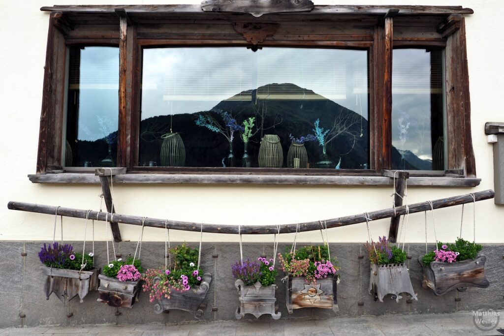 Holzfenster mit Blumenmobile auf gebogener Holzstange