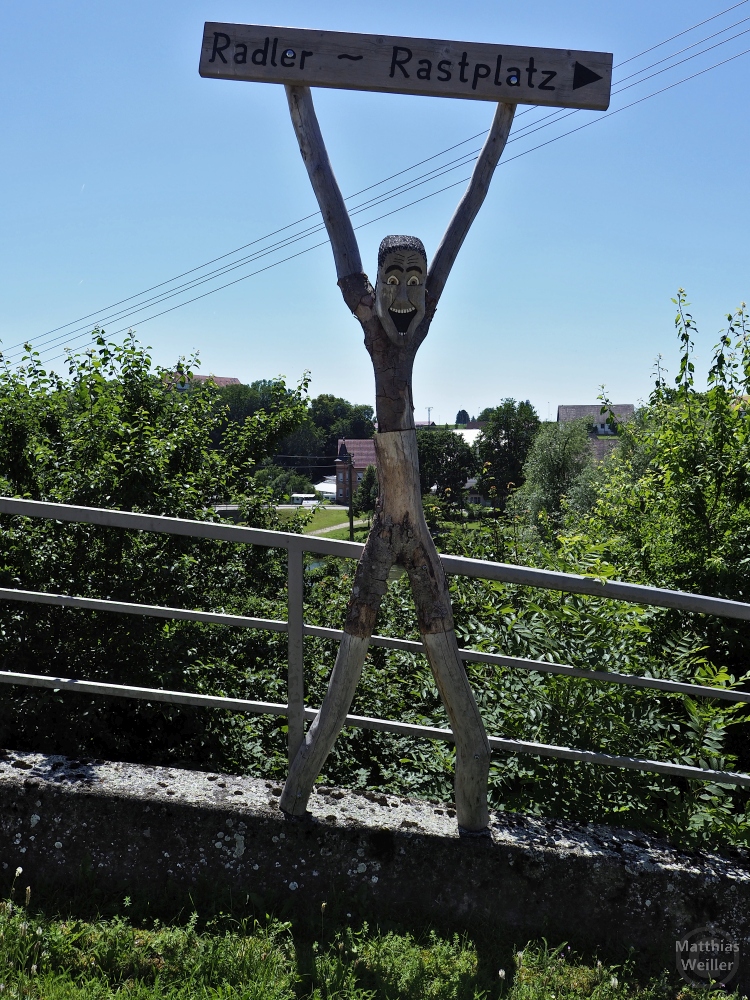 Holzskulptur mit hochgerissene Armen und Hinweis "Radler - Rastplatz"