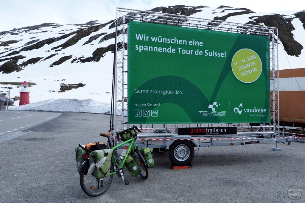 Grünes Werbeschild "Wir wünschen ein spannende Tour de Suisse" mit grünem Reiserad
