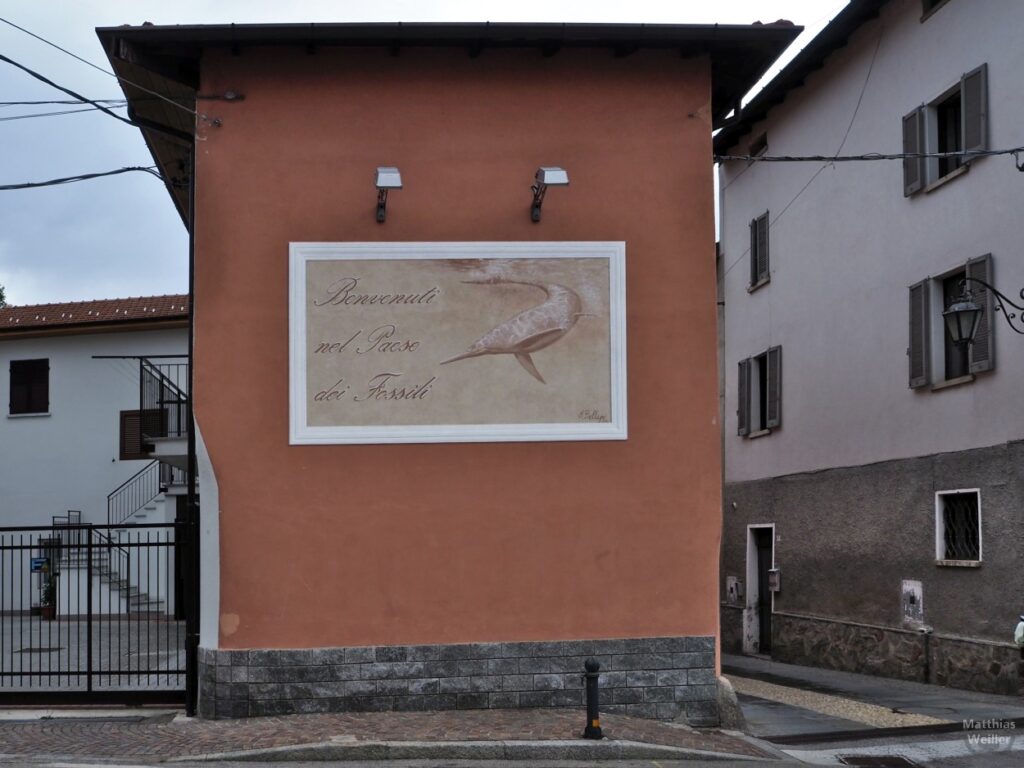Fresko auf Fassade "Benvenuti nel Paese dei Fossili" mit Urzeit-Schwertfisch