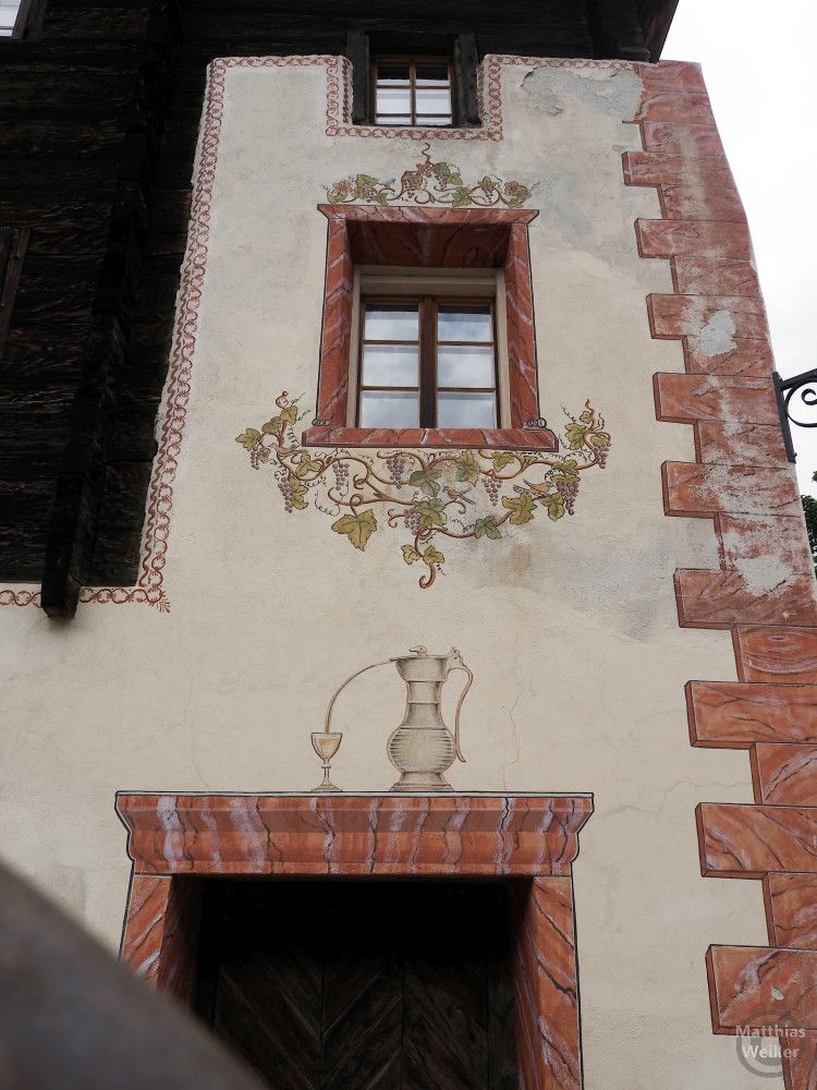 Freskodetail auf Fassade mit Rebendarstellung und Karaffe und Weinglas