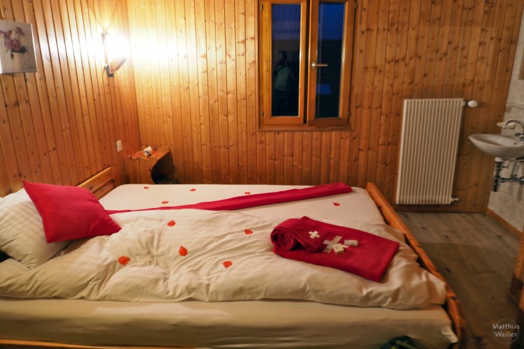Hotelbett im Rot-weiß-Dekor und Blütenblättern