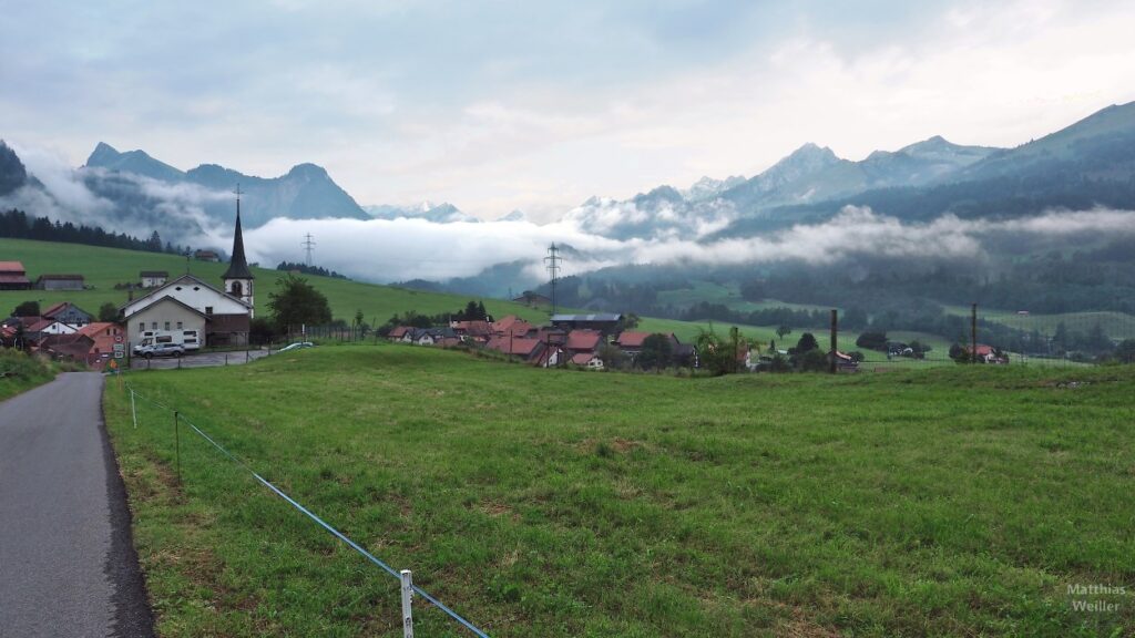 Blick ins Freiburgerland mit Dorf, Weiden, Bergketten und Wolken