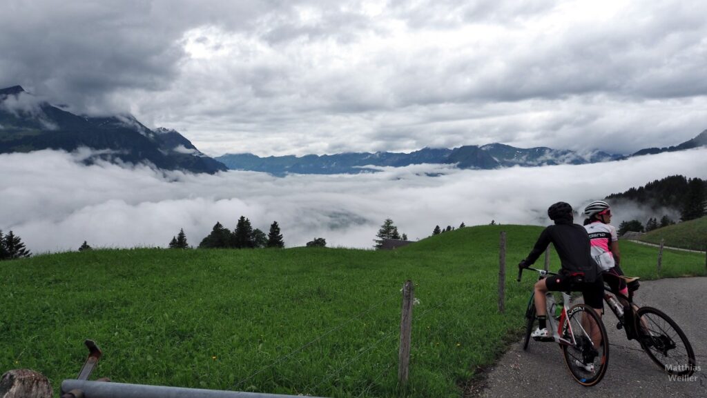 Rennradlerpaar mit Blick über Wolkenmeer zu Gipfelketten