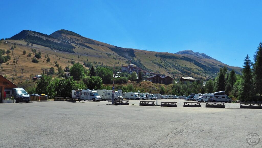 Große Parkfläche mit Campern vor Bergkulisse in Les Deux Alpes