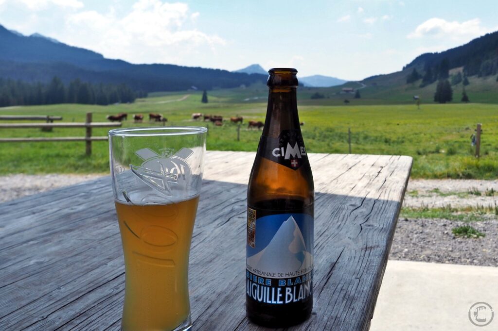 Bierglas mit Bierflasche "Aiguille Blanche" auf Almtisch vor Almweide