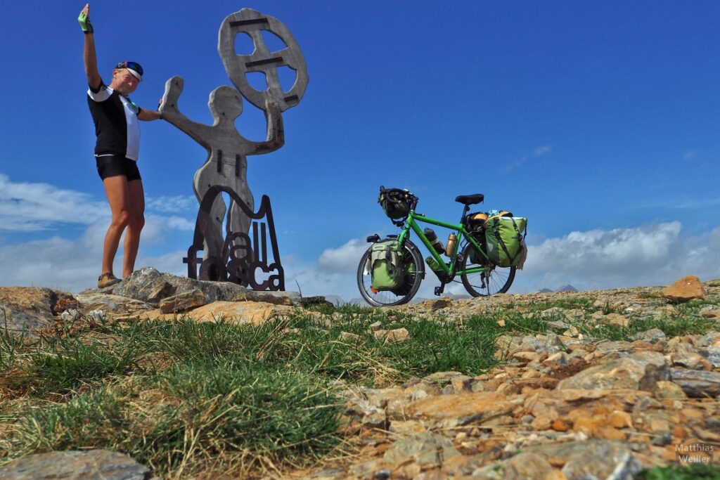 Siegerpose mit Holzskulptur Mensch mit Rad "Vall Fosca", daneben Reiserad, Boden-Froschperspektive, Mirador de Campolongo