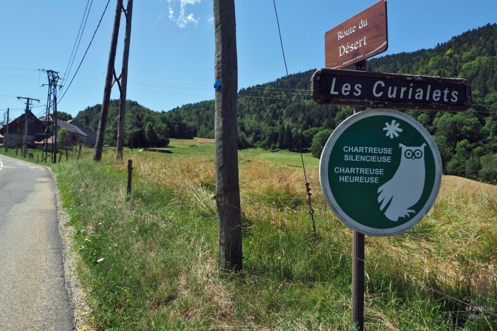 Bergwiesenanfahrt mit Schildern "Les Curialets", "Chartreuse Silencieuse/Chartreuse Heureuse" mit Eulenkarikatur