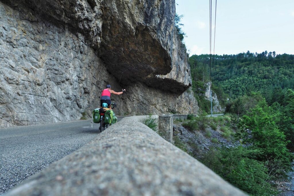 Selbstporträt von hinten Reiserad fahrend unter Felsüberhang über Straße, Gorges de l'Escharis