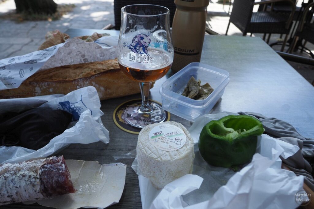 Bierglas "La Bête" auf Tisch mit Eigenversorgung Baguette, Trockenwurst, Ziegenkäse "Mont Aiguoal", grüne Paprika aufgeschnitten, eingelegte Artischocken in Plastikbox