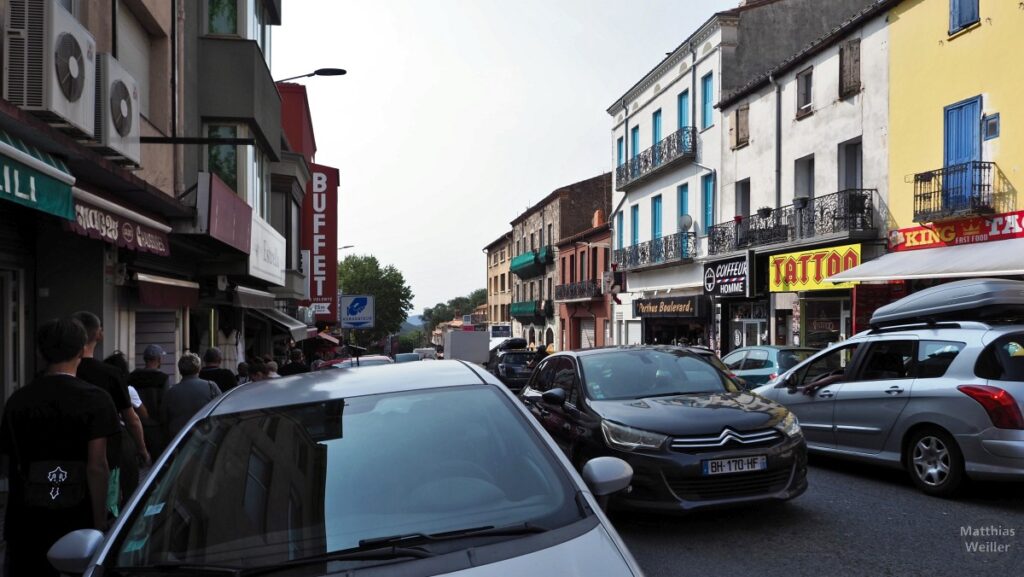 Straßenszene mit dichtem Autoverkehr und Shoppingmeile in Le Perthus