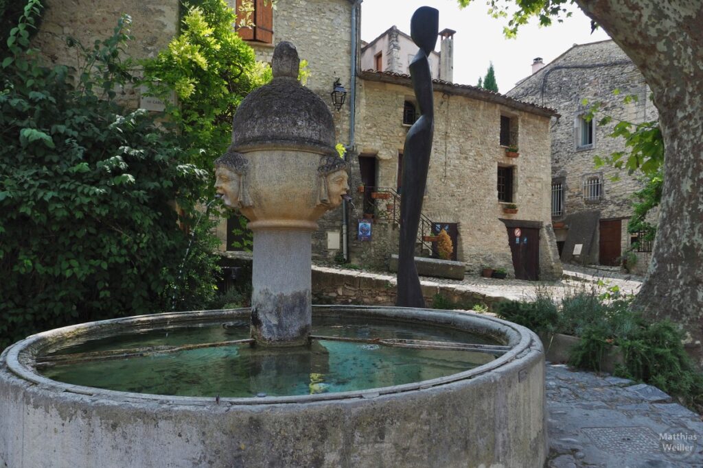 Rundbrunnen mit Spuckköpfen, schlanke, abstrakte Frauenskulptur im Hintergrund, Altstadtecke in Vaison-la-Romaine