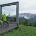 Rahmenblick auf Bergpanorma am Plose, teils in Wolken, mit Velo, Selbstporträt in Regenjacke von hinten