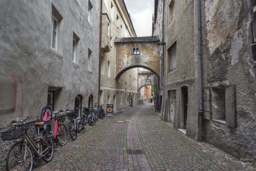 Hinterhofgasse in Bruneck mit Hausbrücke und abgestellten Velos