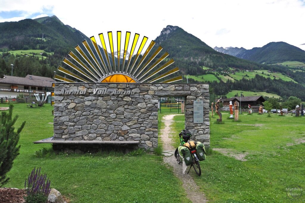 Begrüßungstor aus Steinen mit Halbsonne aus Kunststoff darüber "Ahrntal Valle Aurina", mit Velo