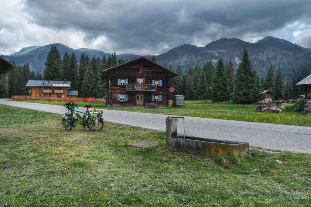 Brunnen und Velo vor Berghäusern und Bergkulisse