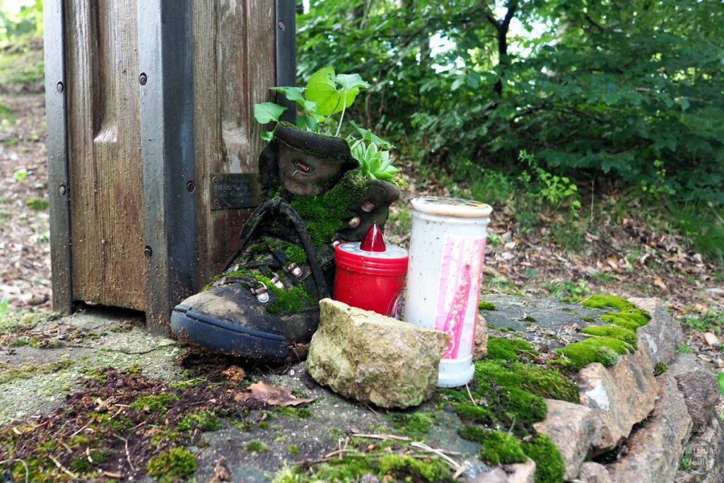 bemooster Schuh neben Grablichtern