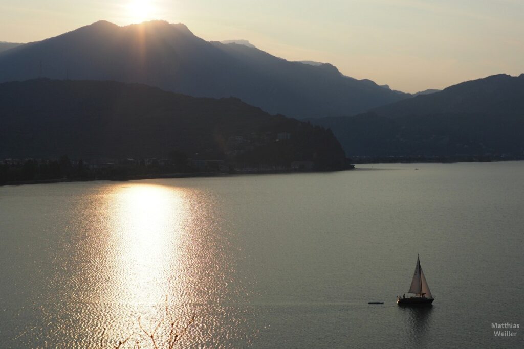 Sonnenaufgang am Gardasee im Gegenlicht, mit Segelboot