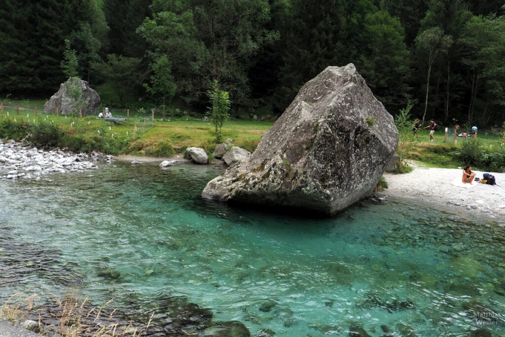 Blockstein an türkisfarbenen Bergbach mit kleinem Strand, Leute