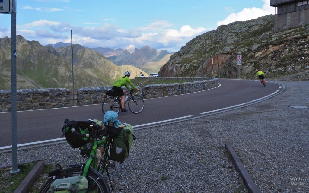 Kurve mit Rennradlerpaar vor Bergkulisse Timmelsjoch, mit Velo