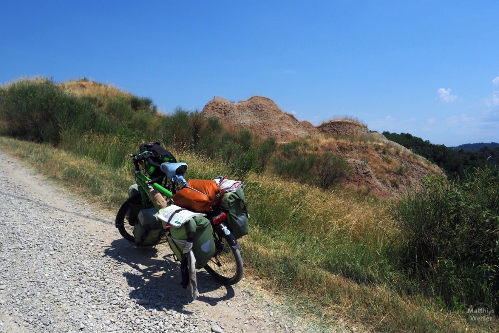 Rötliche Erdhügel neben Piste, mit Reisevelo