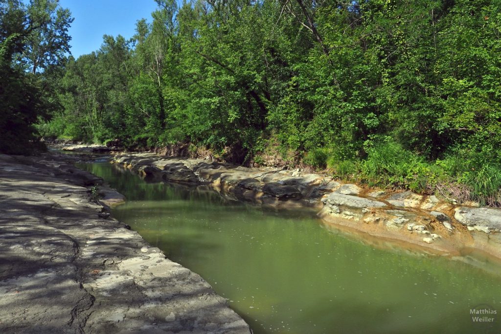 trüber Flusslauf mit Steinplattenufer
